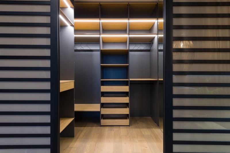 Walk-in wardrobe with wooden shelving, hanging rails and warm lighting